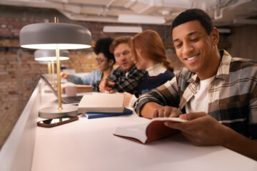 Na imagem aparecem estudantes em uma bancada interagindo e com livros abertos.
